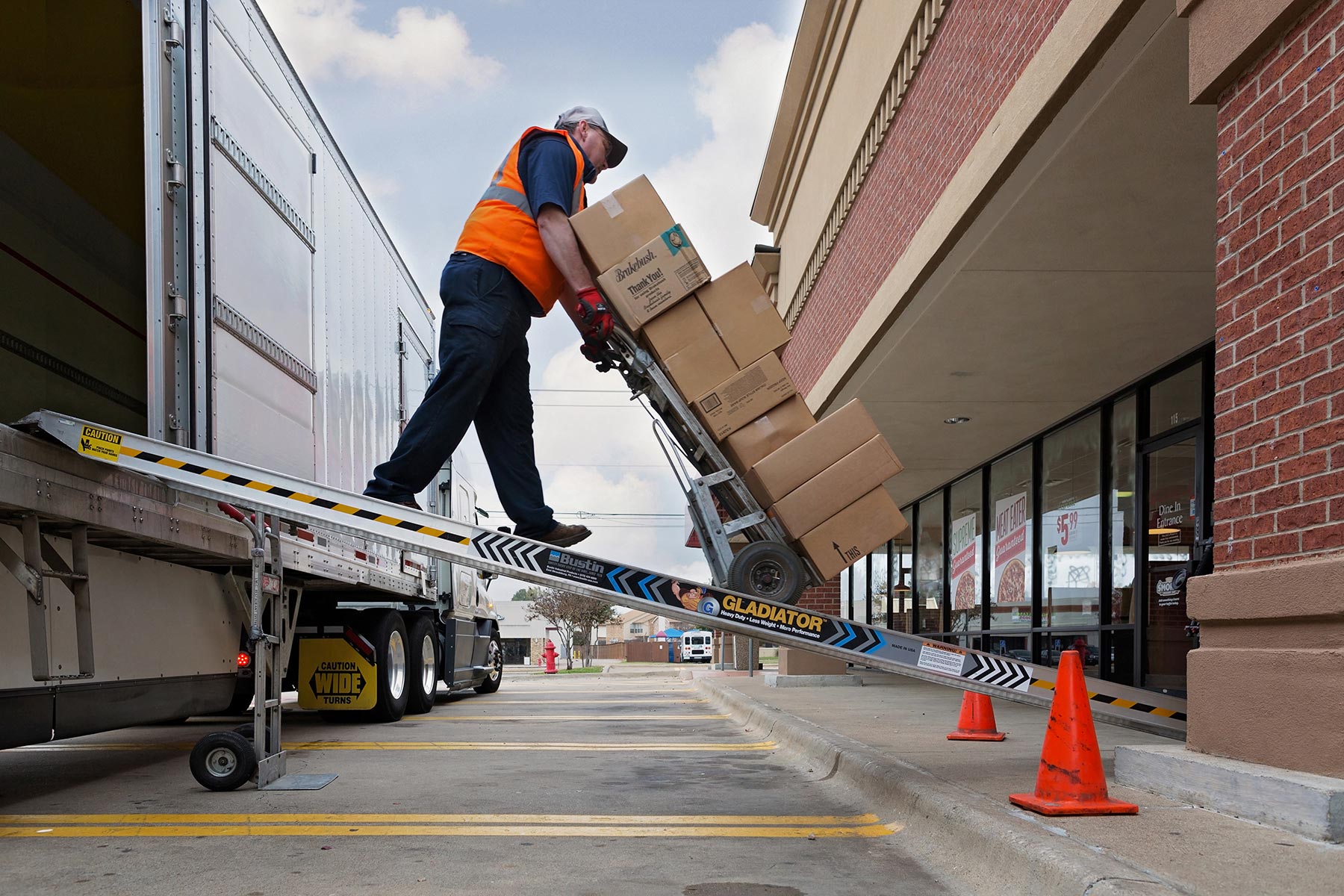 Man with a tall stack of boxes on a hand truck moving down a ramp from a truck